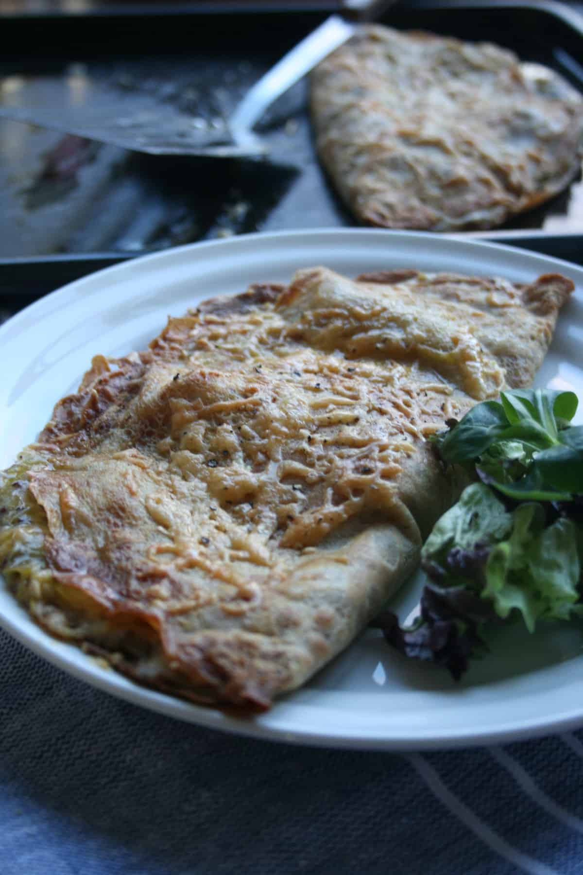 A close up of a cheesy topped pancake with salad to the side.