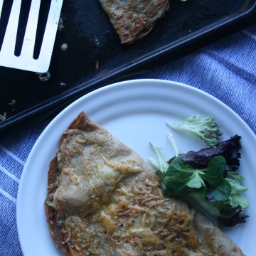 A plate with a savoury pancake on it with salad to the side and spatula above.