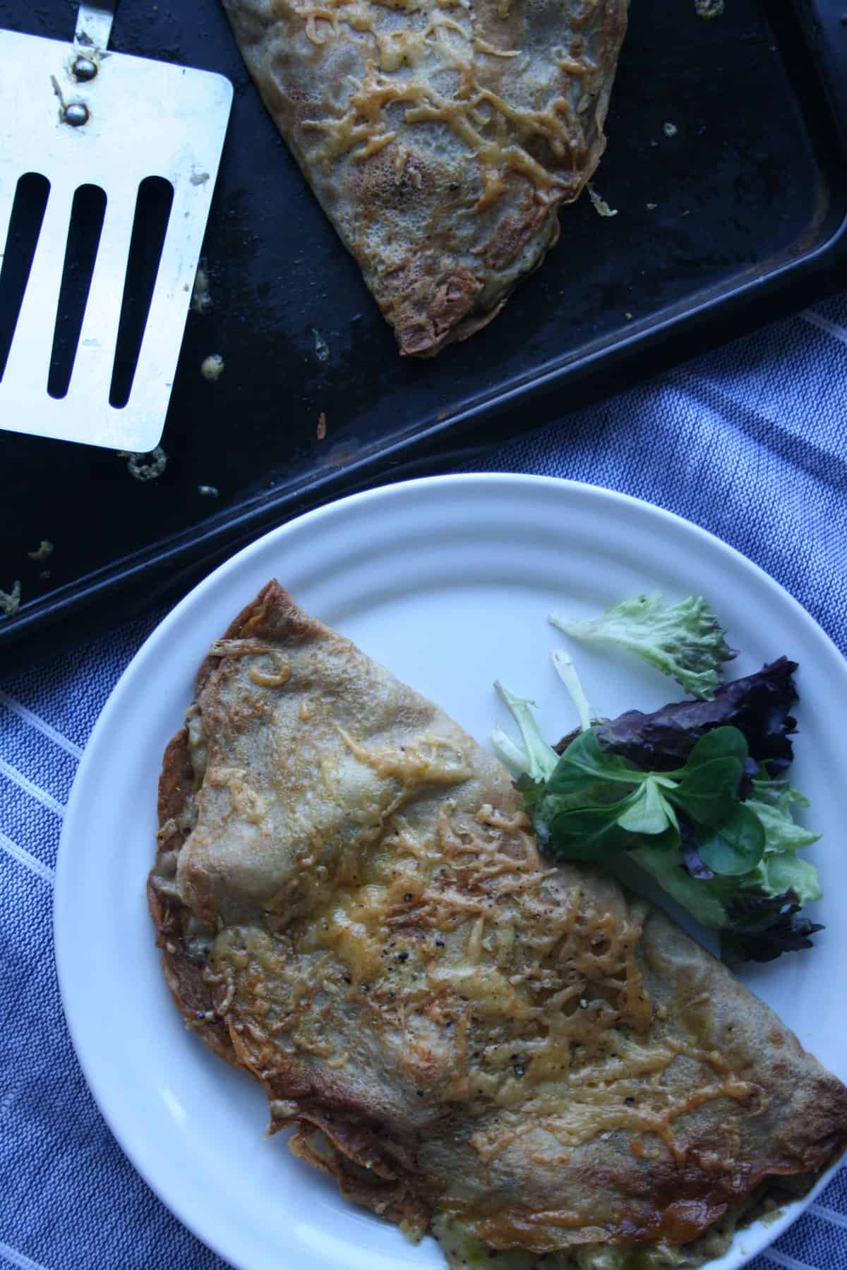 A plate with crepe and salad with a spatula to the top.