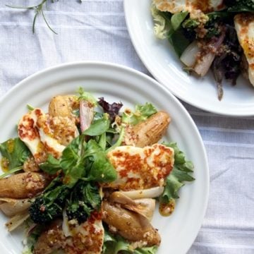 A plate with roasted shallot and potato salad with grilled halloumi on top.