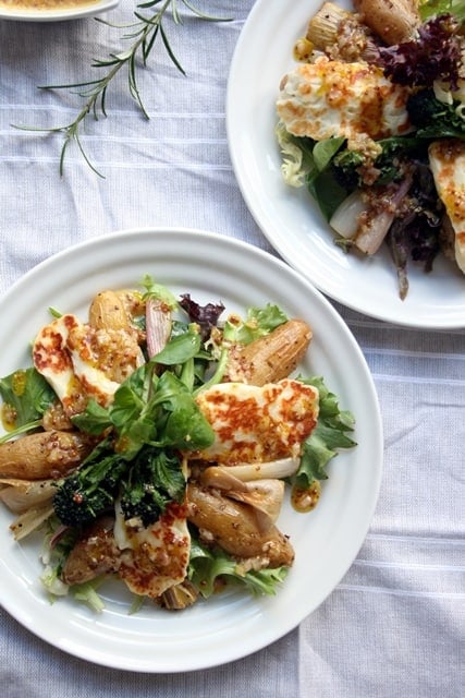 A plate with roasted shallot and potato salad with grilled halloumi on top.