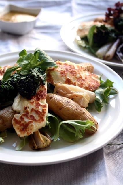 A plate of roasted potato and shallot salad with grilled halloumi on top.