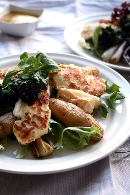 A plate of roasted potato and shallot salad with grilled halloumi on top.