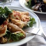 A plate of grilled halloumi on top of potato and shallot salad with a fork.