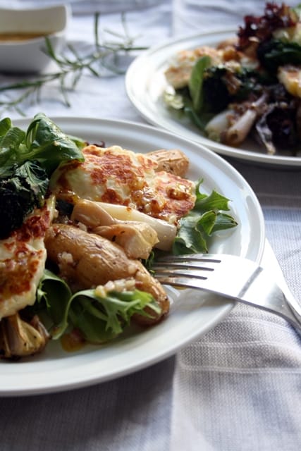 A plate of grilled halloumi on top of potato and shallot salad with a fork.