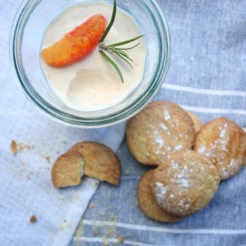 A glass with orange posset and biscuits to the side.