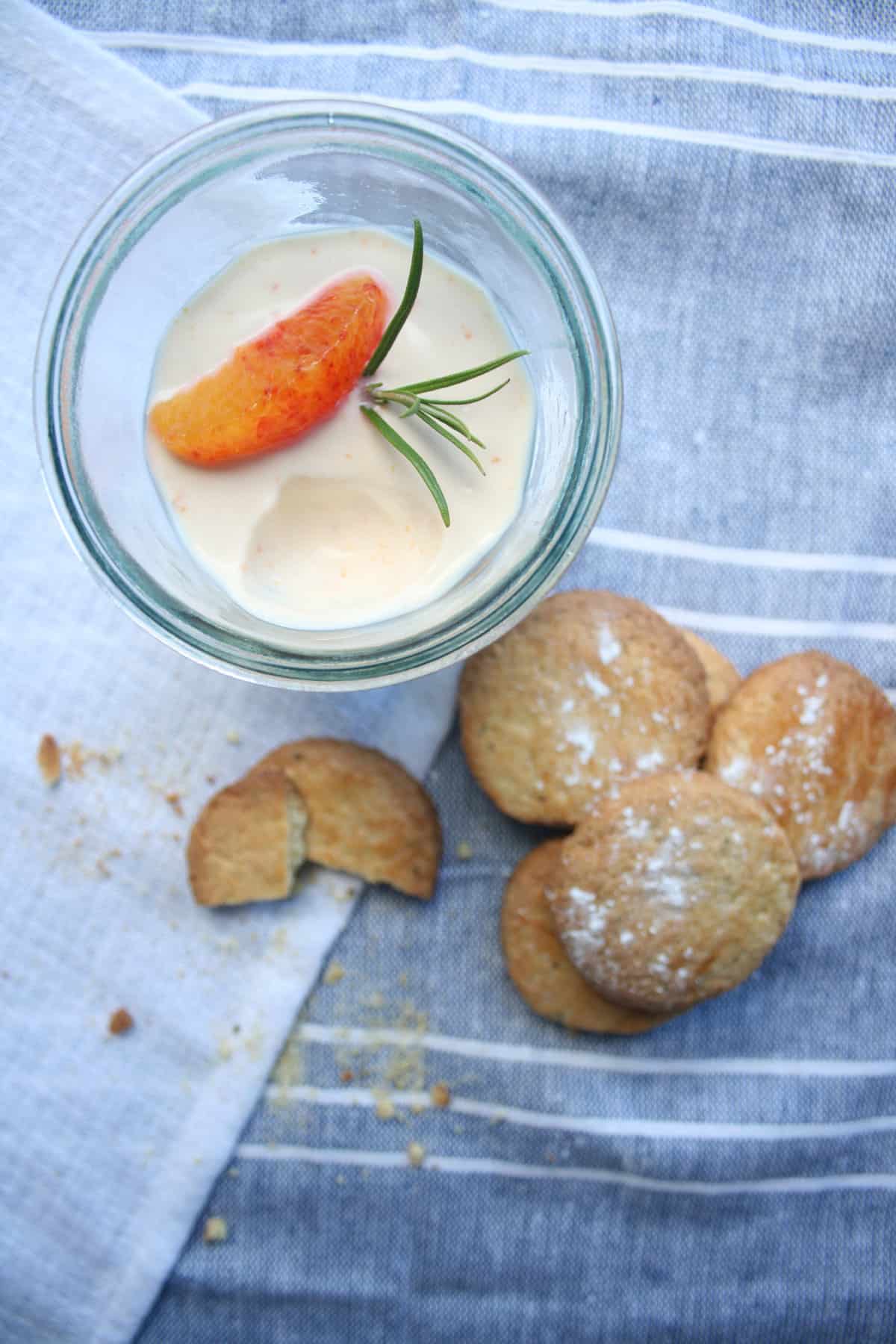 A glass with orange posset with a scoop taken and biscuits to the side.