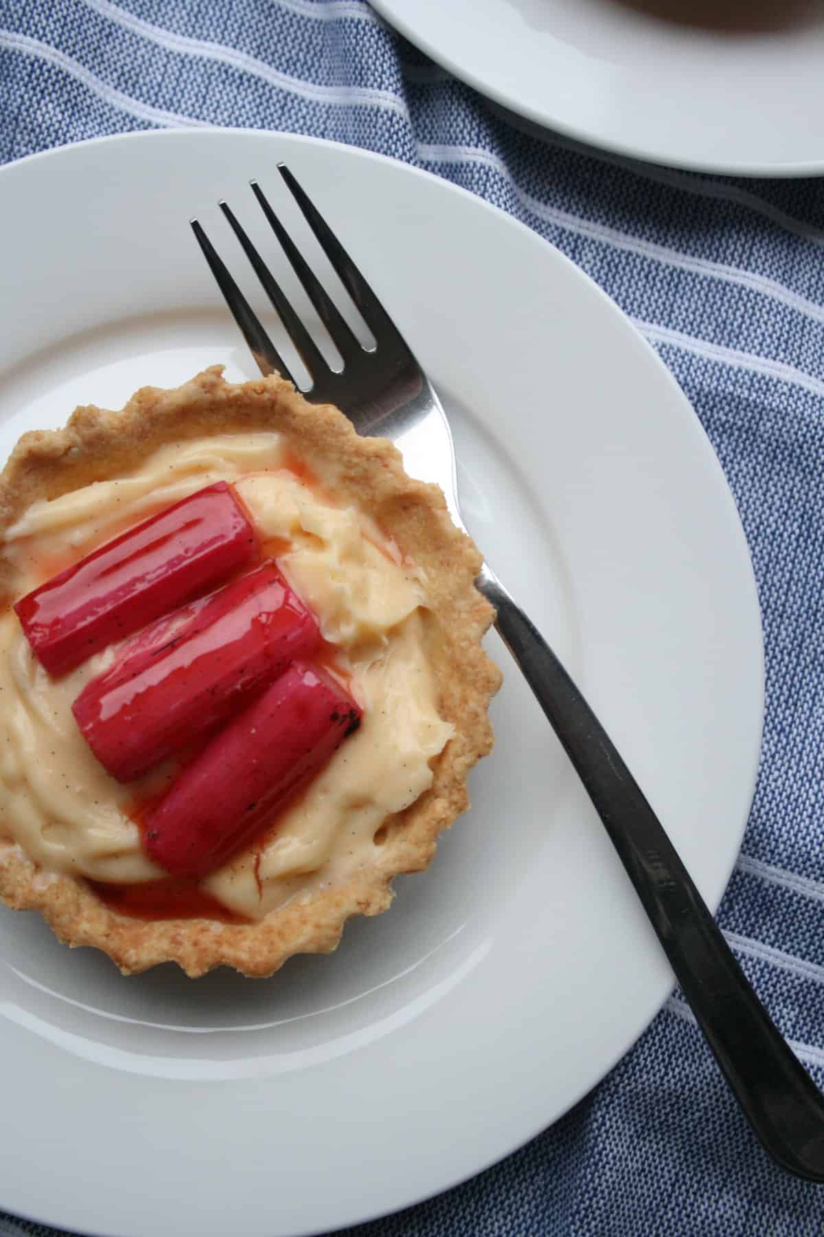 A plate with rhubarb custard tart on top with a fork and napkin underneath.