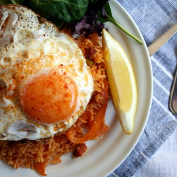 A plate with paella and fried egg on top, lemon wedge on top.