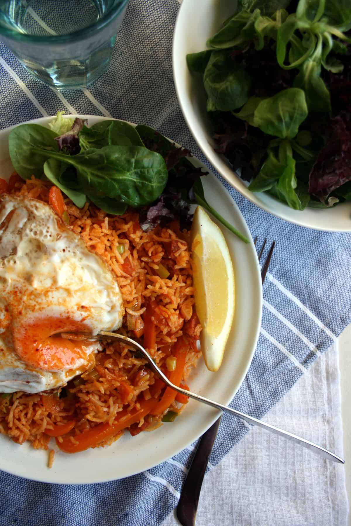 A plate of paella with a fried egg on top and fork with salad to the side.