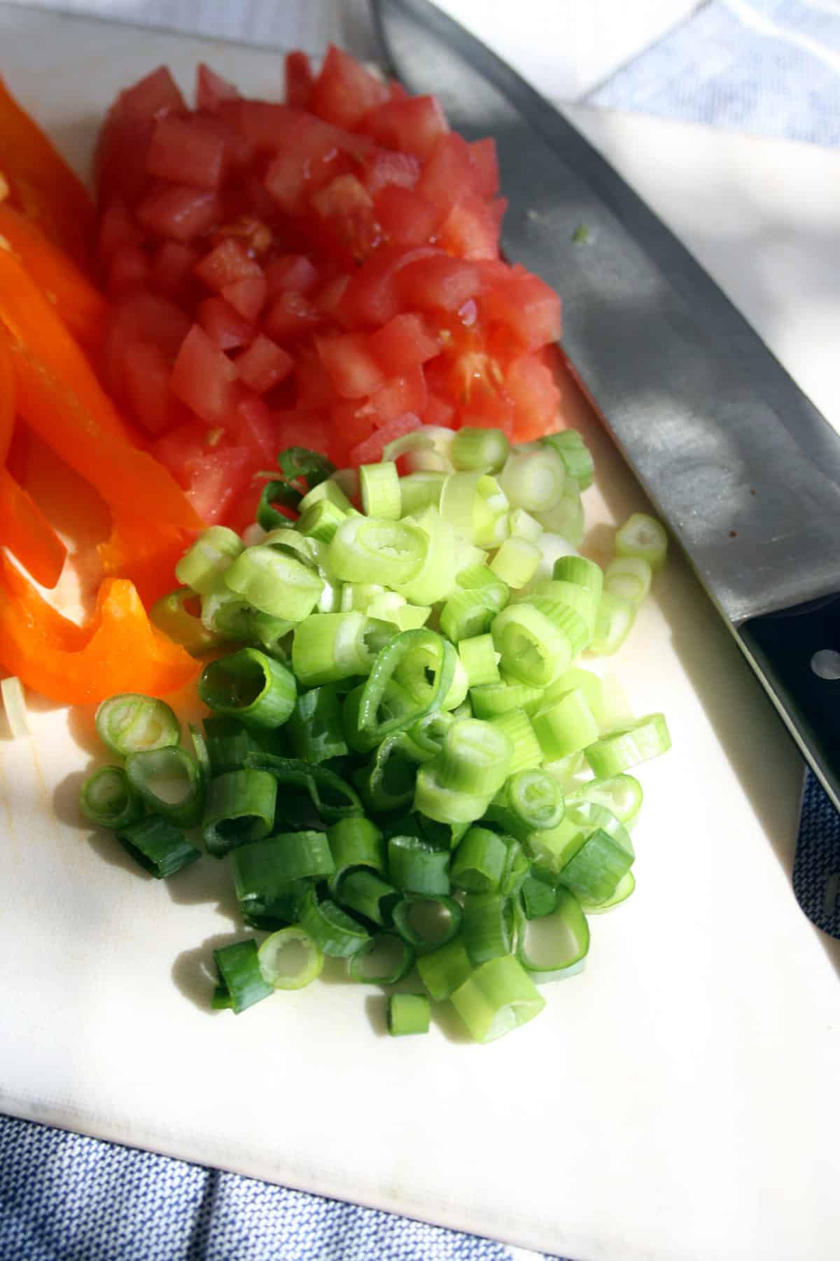 Chopped green onions, pepper and tomatoes with a knife.