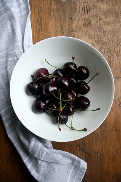 A bowl of cherries with a napkin and a wooden background.