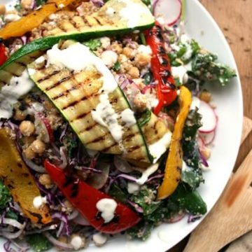 A plate of chargrilled vegetables on a quinoa salad with a creamy dressing dressed over.