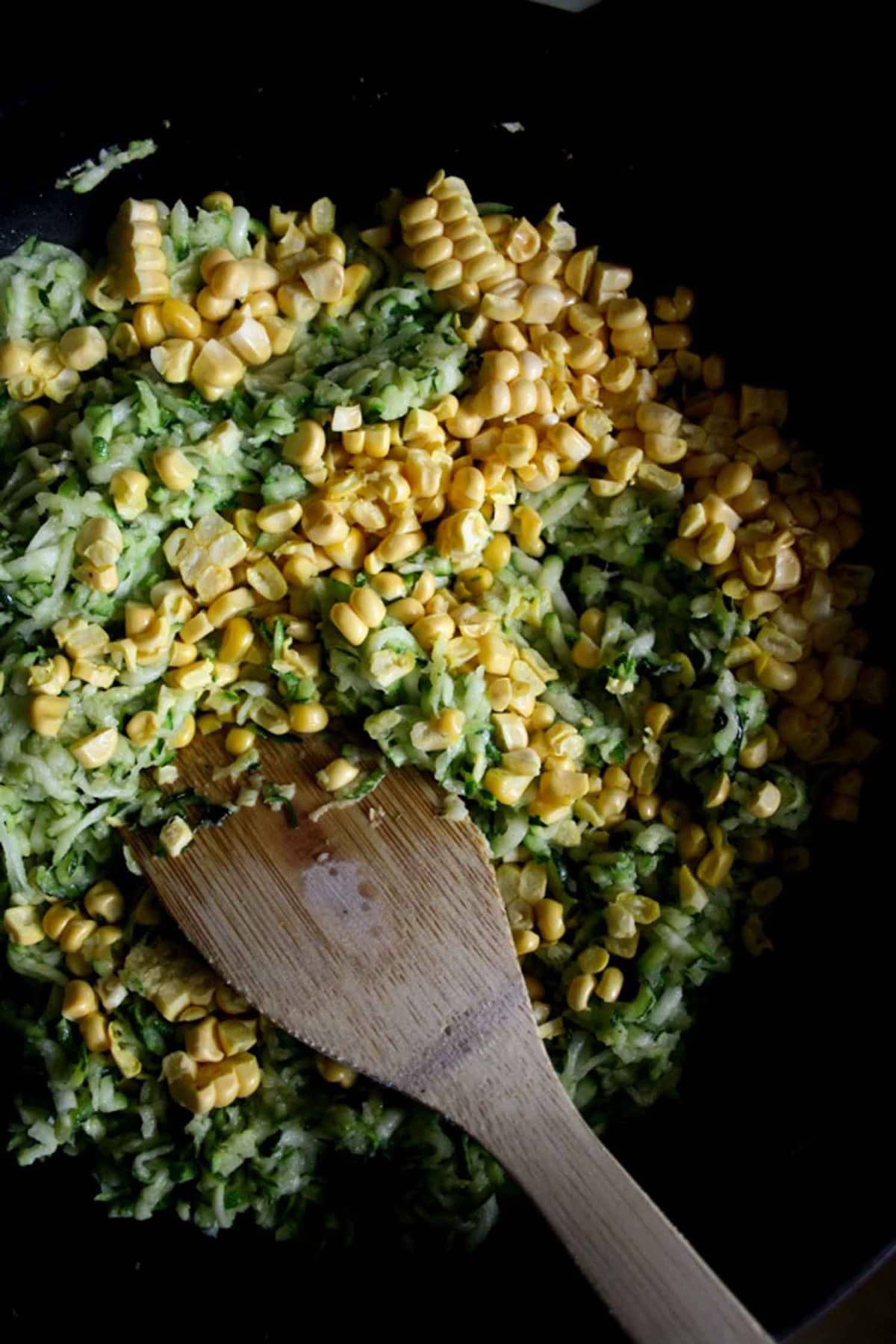 Courgette and sweetcorn tart filling in a skillet with a wooden spatula