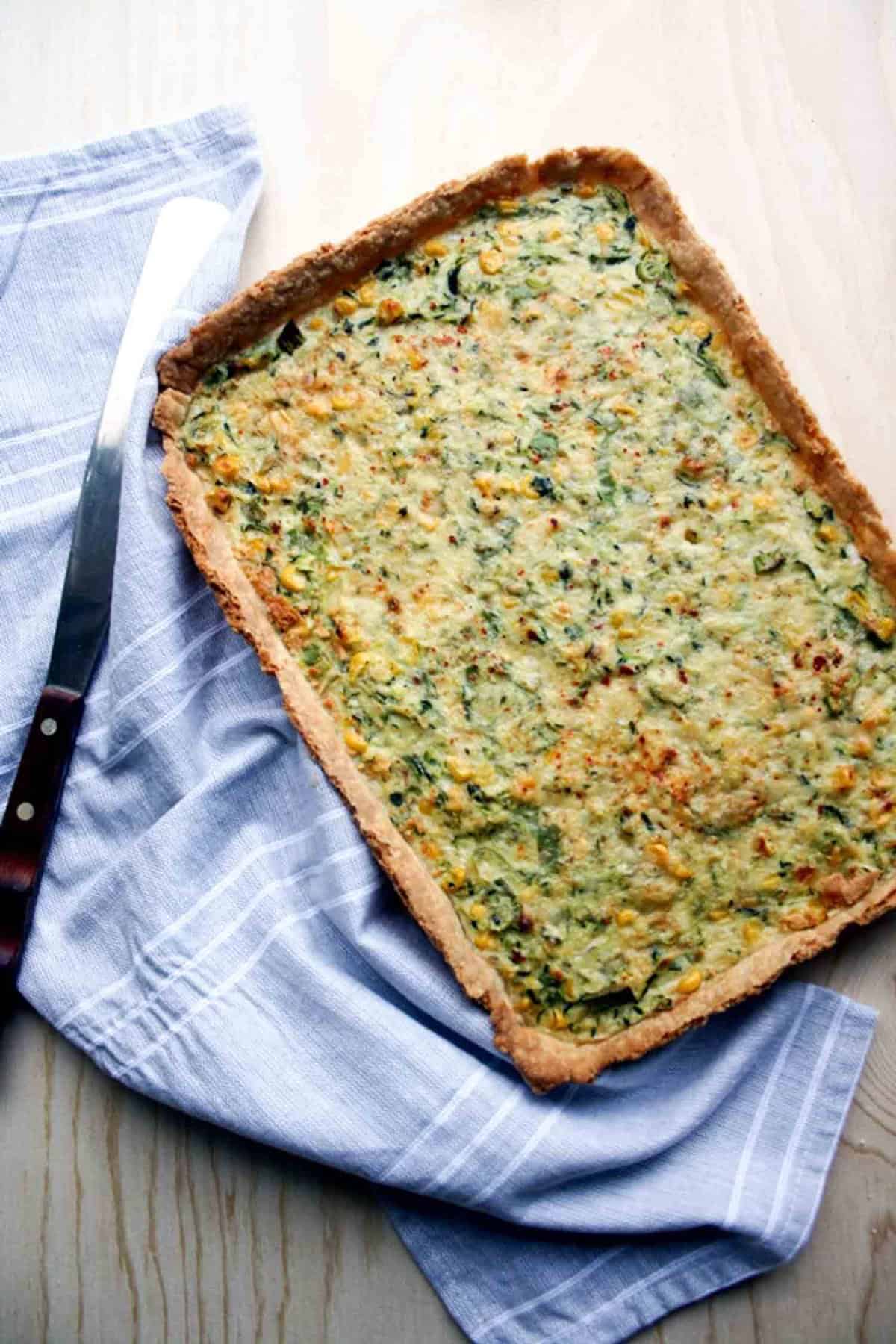 A courgette and corn tart with a napkin and spatula to the side.