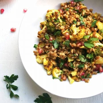 A plate of roasted cauliflower farro salad in a bowl with herbs scattered around.