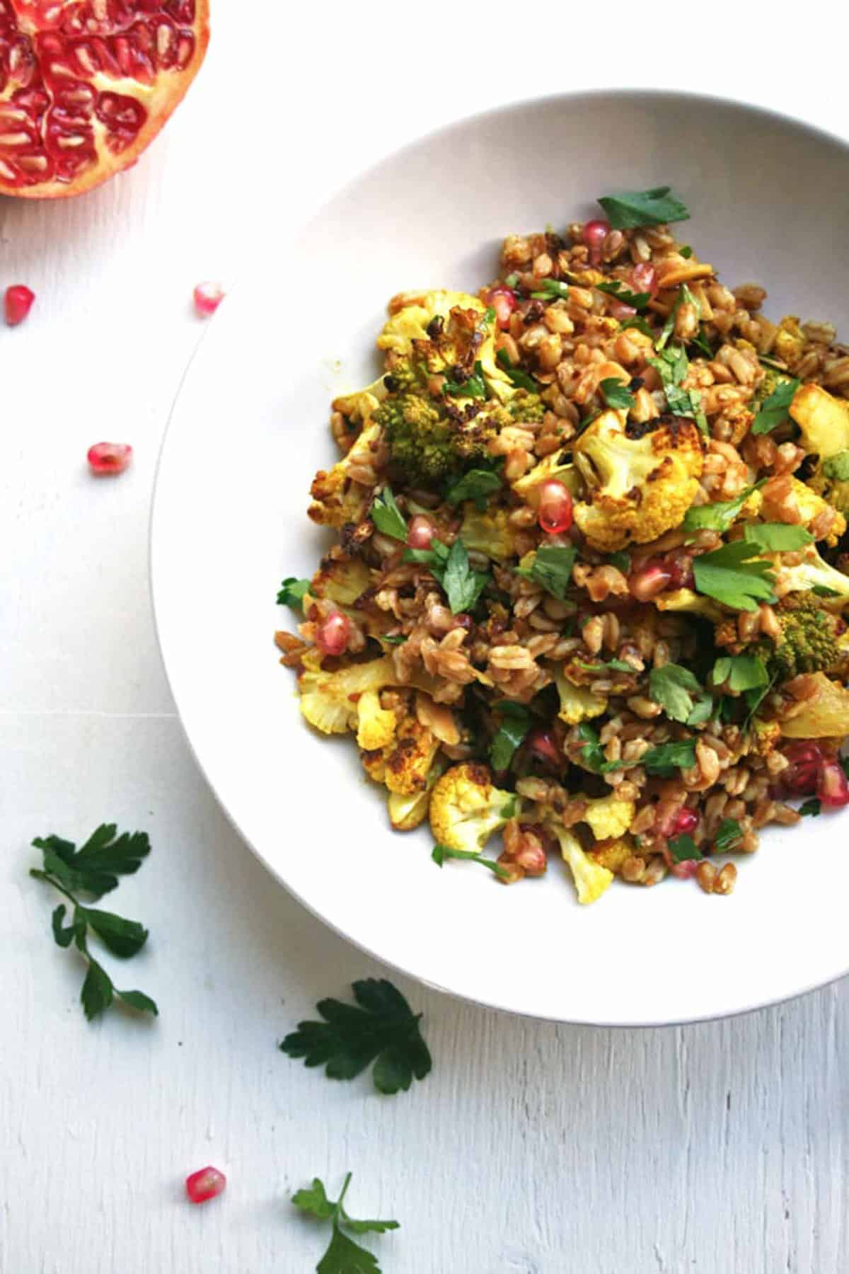 A plate of roasted cauliflower farro salad in a bowl with herbs scattered around.