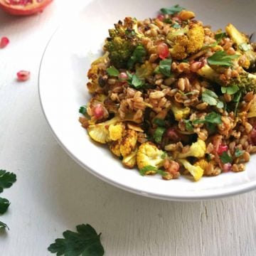 A bowl of roasted cauliflower farro salad with herbs around.