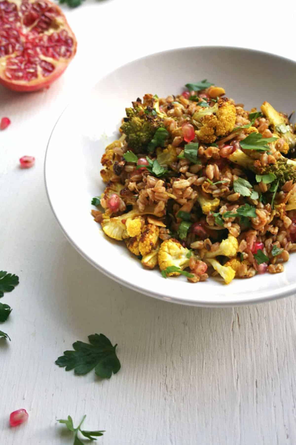 A bowl of roasted cauliflower farro salad with herbs around.