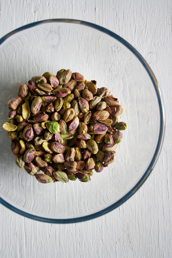 A glass bowl with raw pistachios shelled inside.