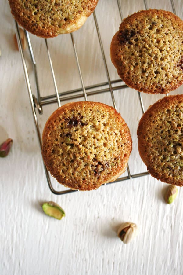 Three frangipane tartlets on a cooling rack with pistachios around. 