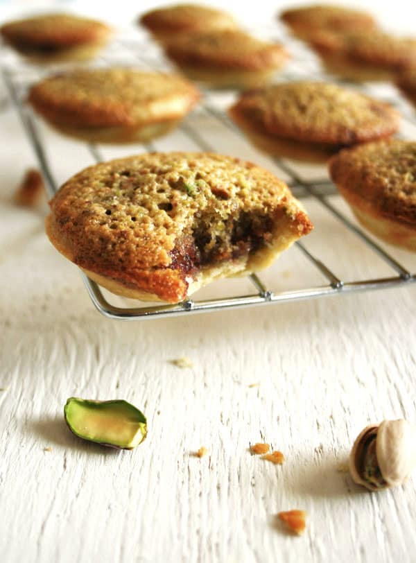 Close up of a bite taken out of a pistachio frangipane tartlet on a cooling rack.