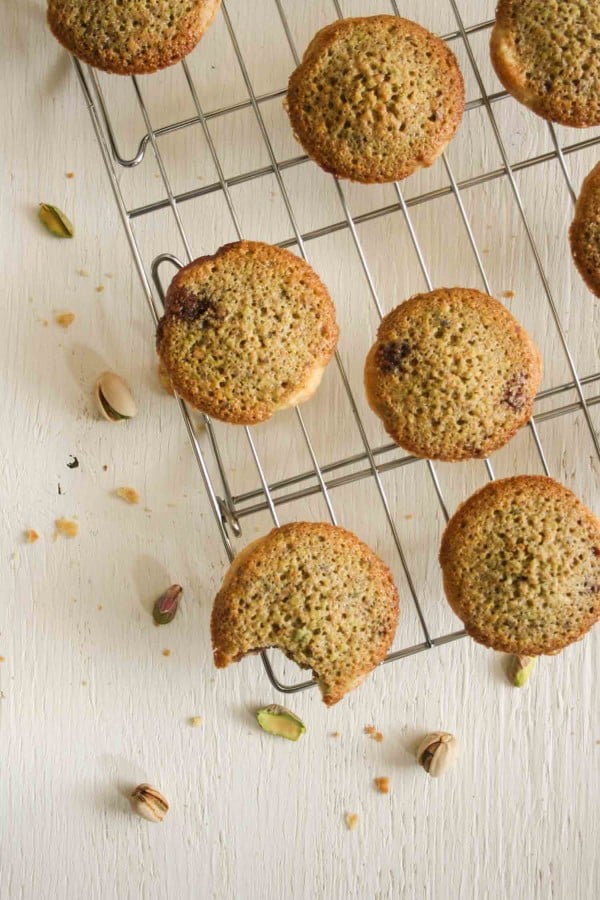 Mini pistachio frangipane tartlets on a cooling rack with nuts around.