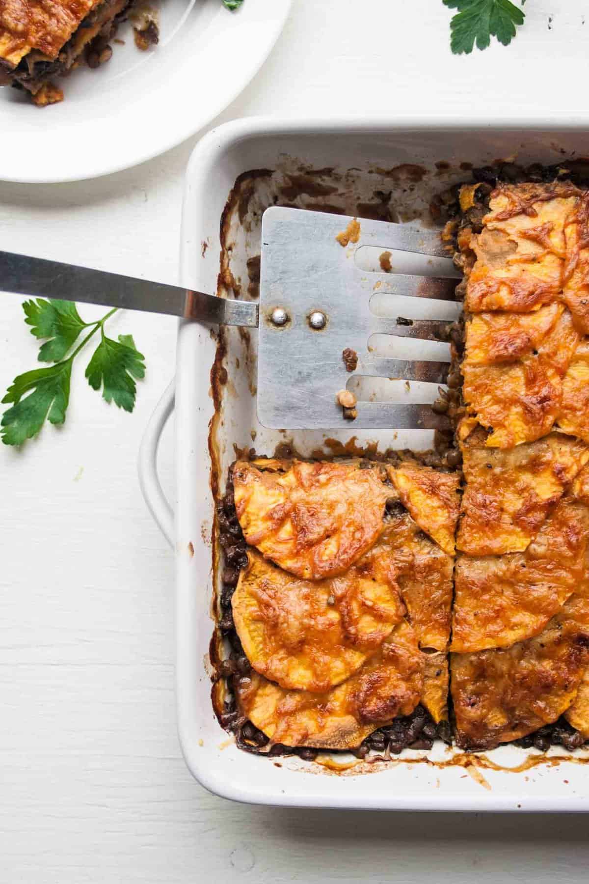 A spatula serving up sweet potato lentil lasagne slice from a dish.