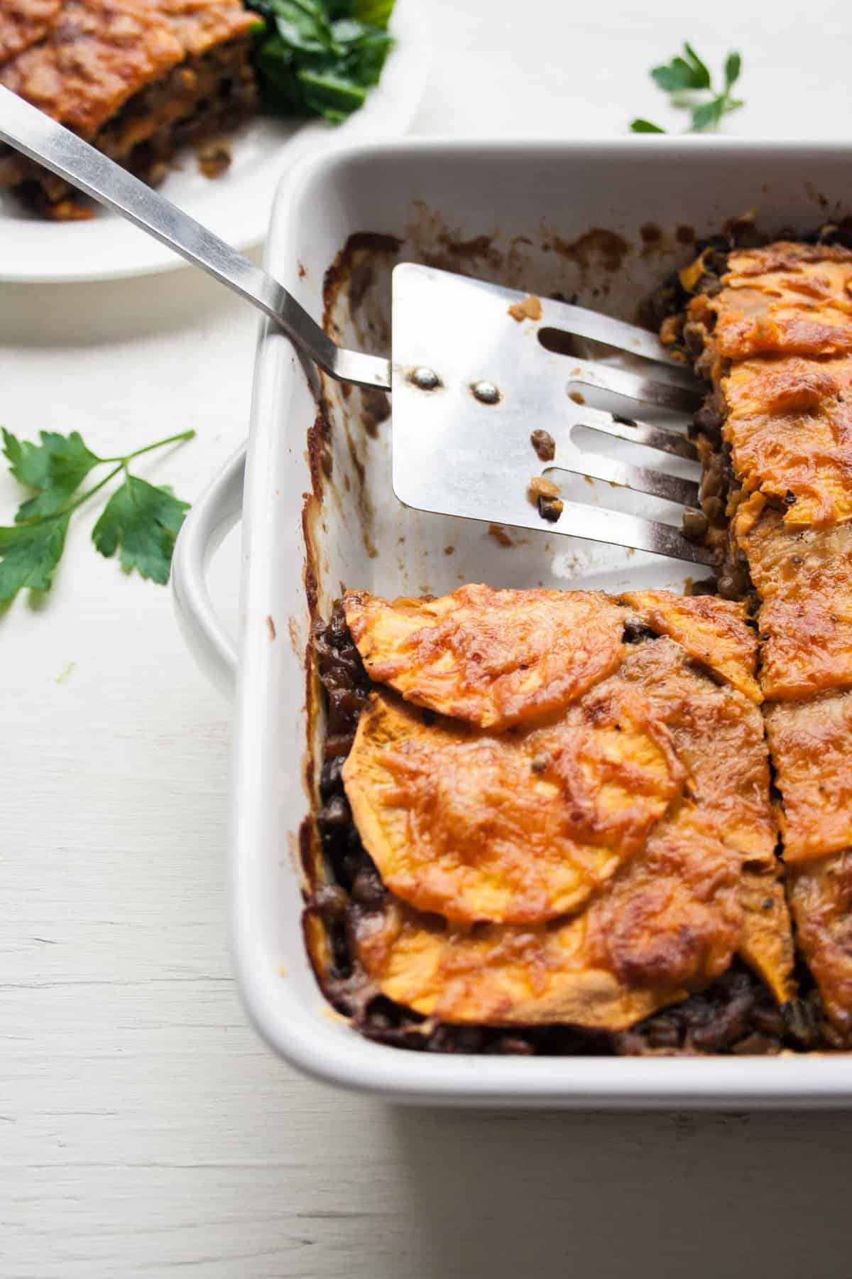 A spatula serving the sweet potato lentil lasagne from a dish.