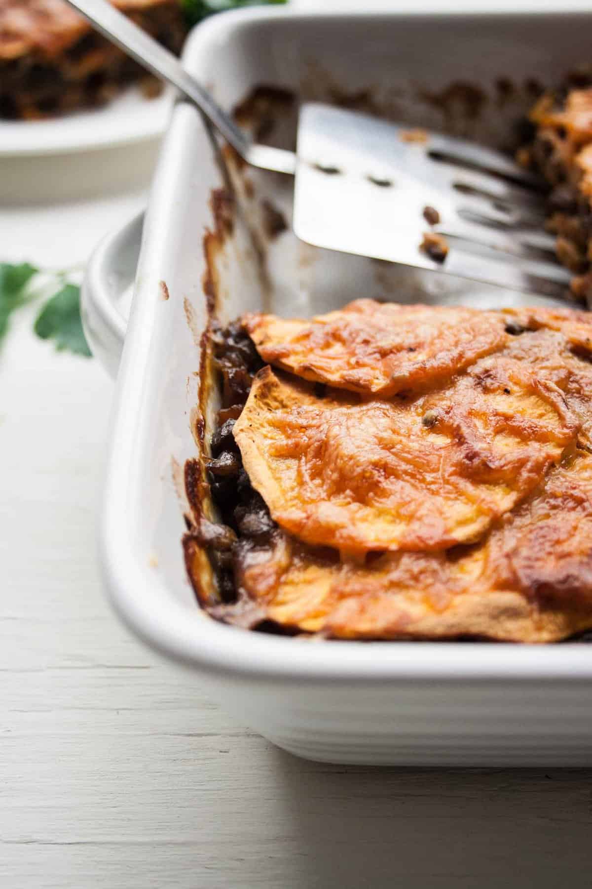 A close up of a lentil sweet potato lasagne with a spatula behind.