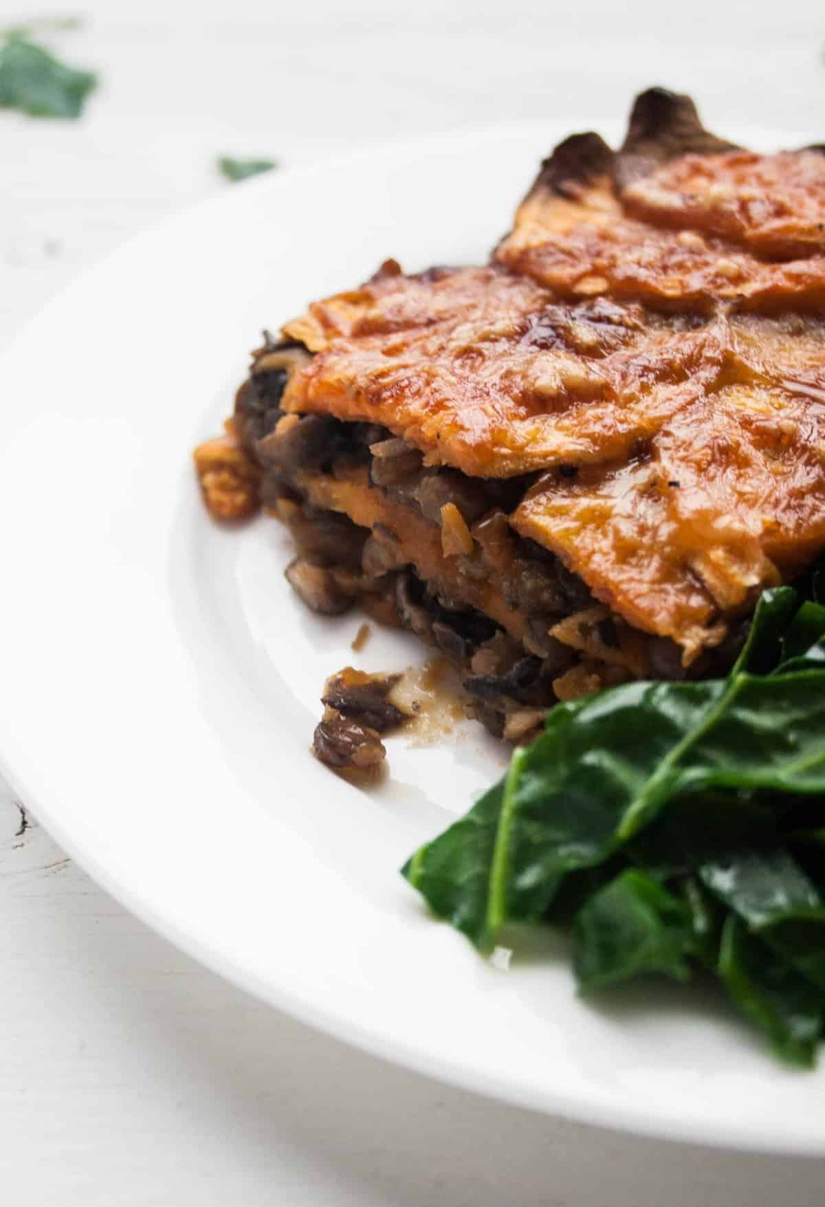 A serving of lentil and sweet potato lasagne on a plate with greens to the side.