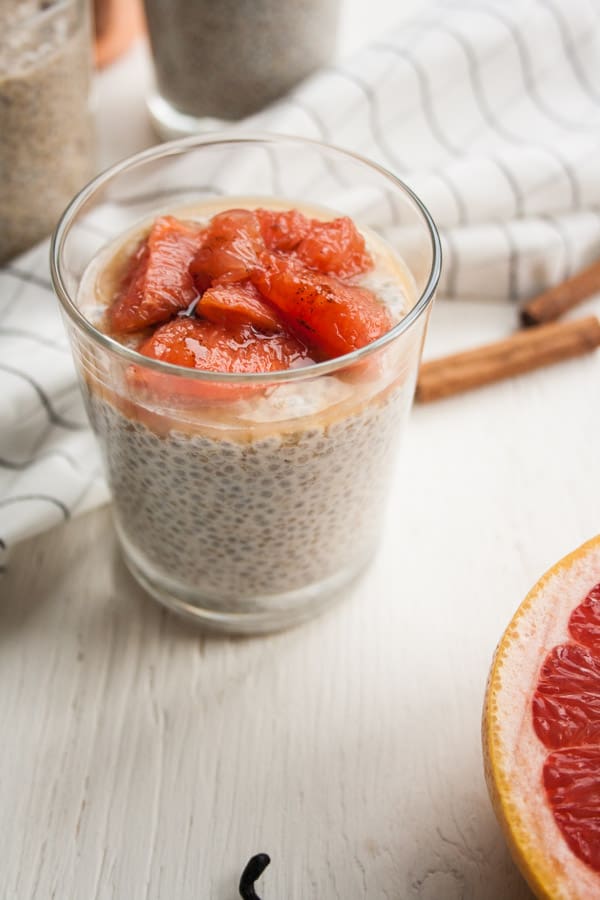A glass of chia pudding with fruit topping in and cinnamon sticks behind.