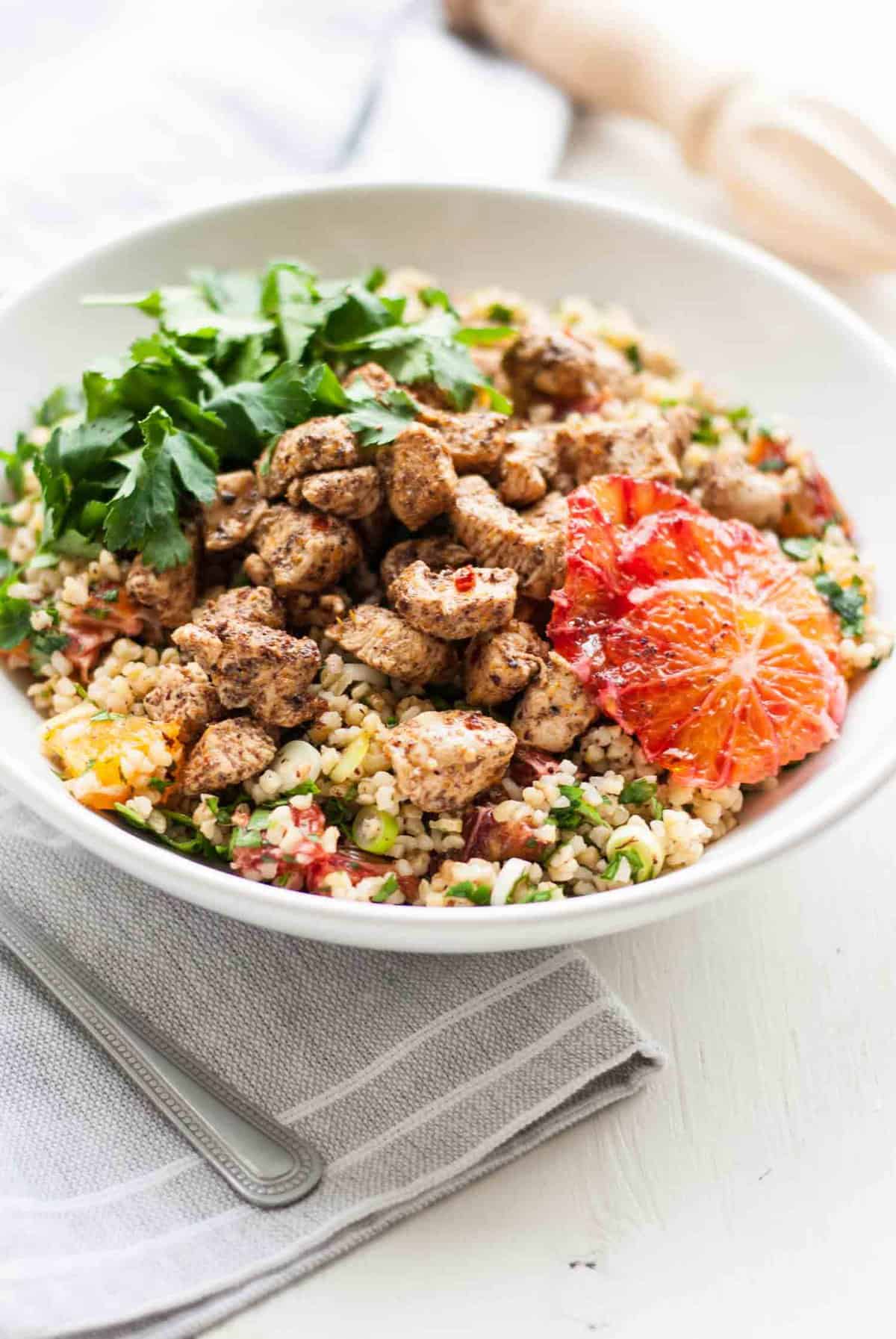 A chicken tabbouleh salad bowl with herbs and orange slices on top.