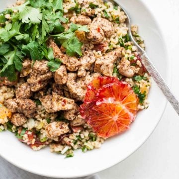 A bowl with chicken, tabbouleh, herbs and slices of orange.