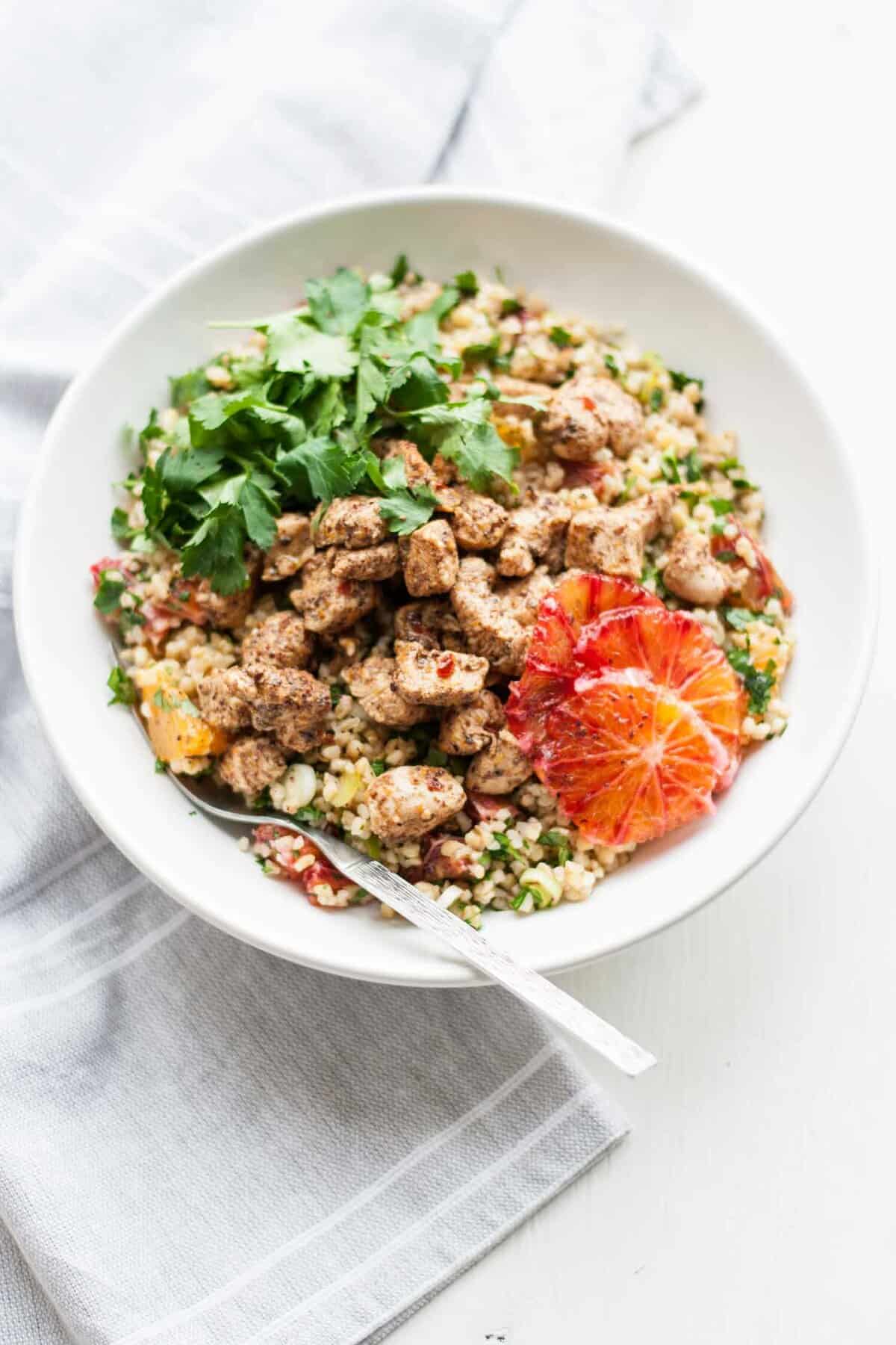 A chicken tabbouleh with herbs and orange slices with a fork.