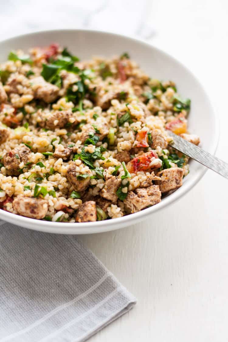 A messed up bowl of chicken tabbouleh with a fork.