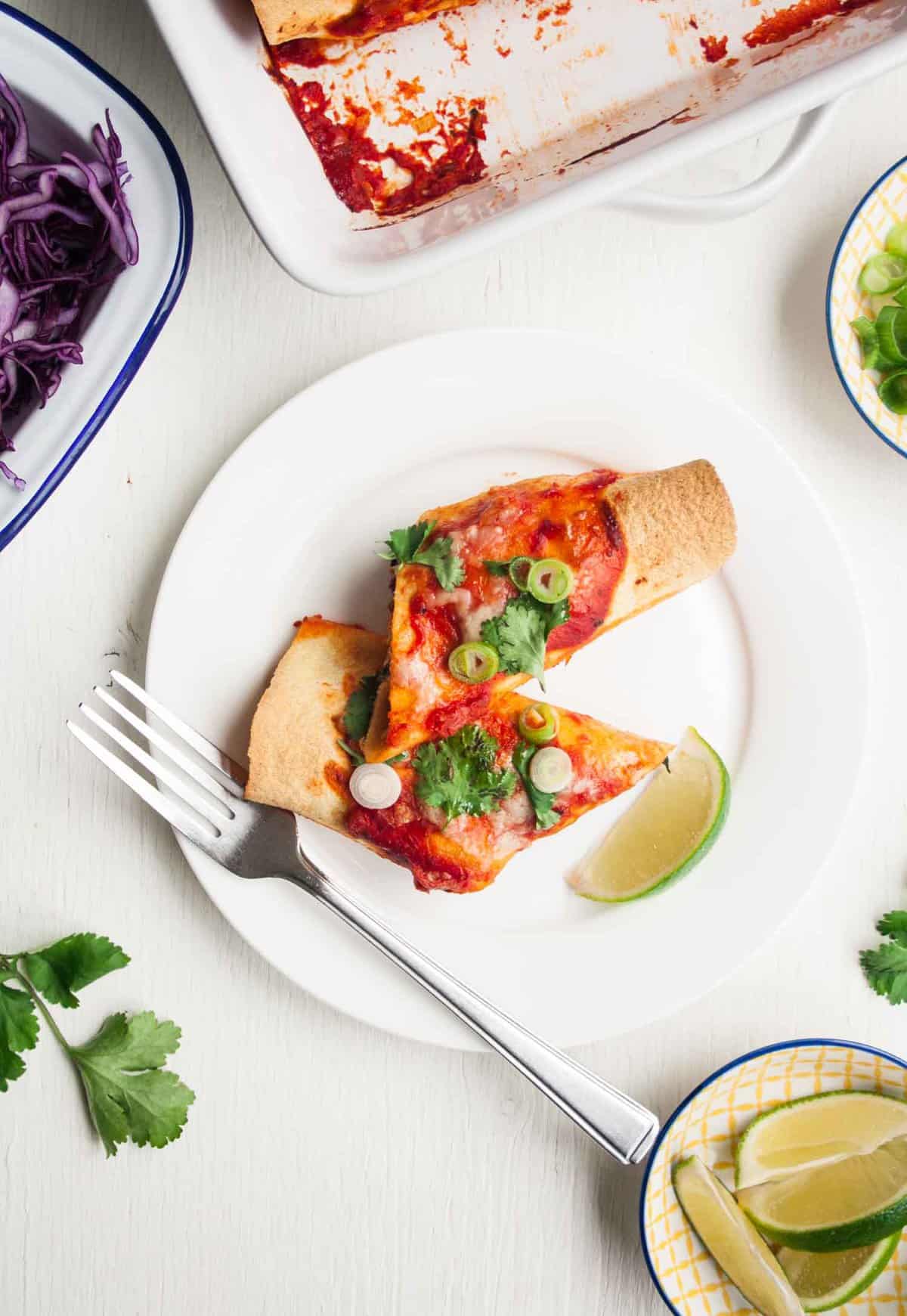 A plate with enchilada on it with a lime wedge with a fork.