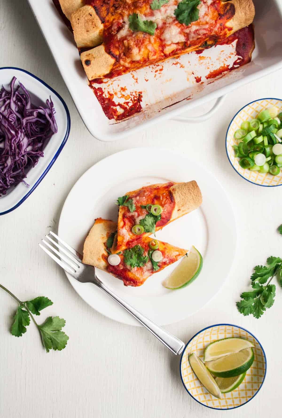 A plate with an enchilada cut in half with a fork and slaw to the side.