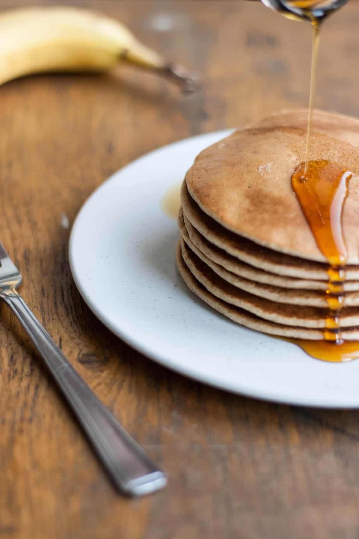 A plate with a stack of pancakes with a drizzle of maple syrup over the top.