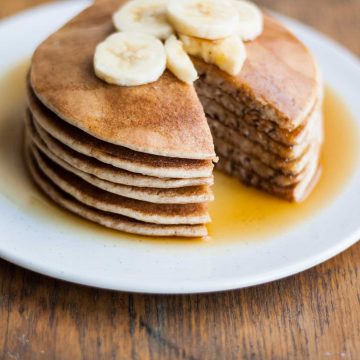 A stack of pancakes with a wedge cut out with banana slices and maple syrup.