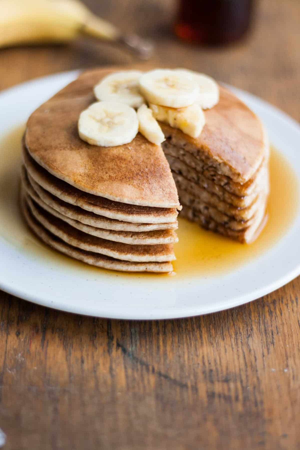 A stack of pancakes with a wedge cut out with banana slices and maple syrup.