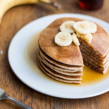 A plate with a stack of pancakes topped with banana slices and a wedge cut.