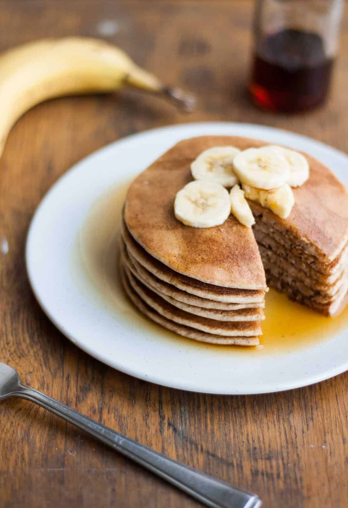 A plate with a stack of pancakes topped with banana slices and a wedge cut.