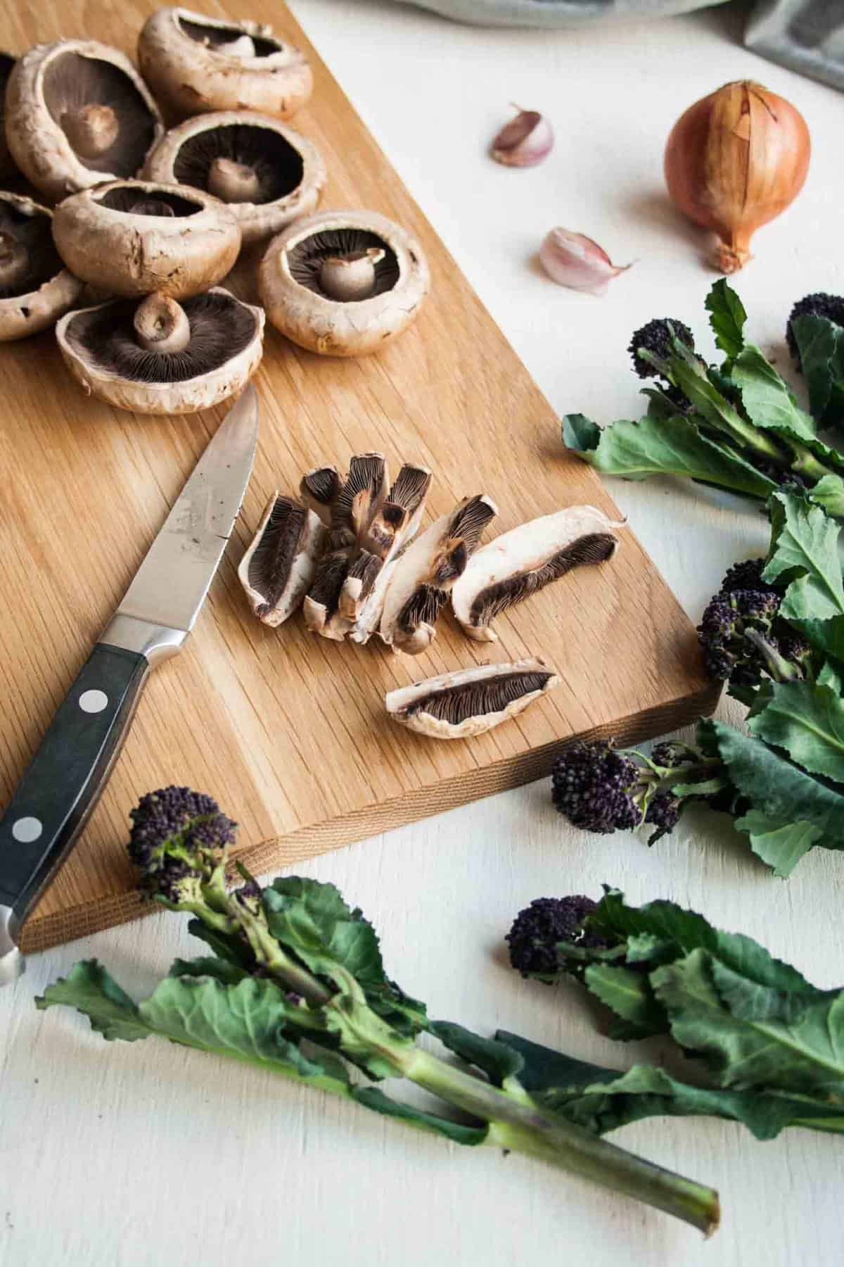 A wooden board with mushrooms being sliced up with a knife to the side.