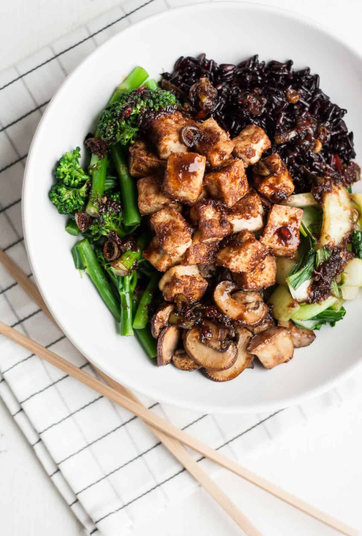 A plate of crispy tofu with broccoli, black rice and mushrooms.