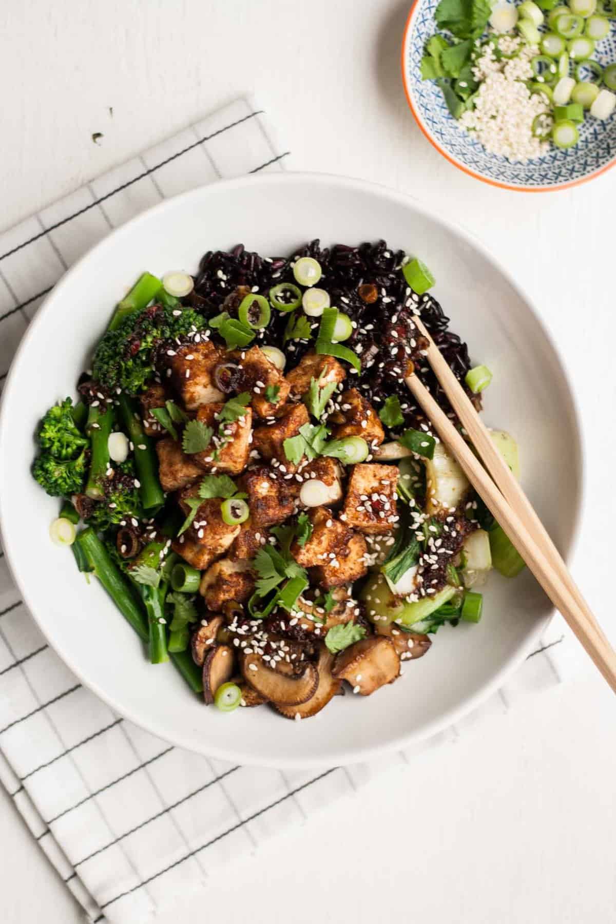 Crispy tofu in a white bowl with black rice on top of a napkin with chopsticks.