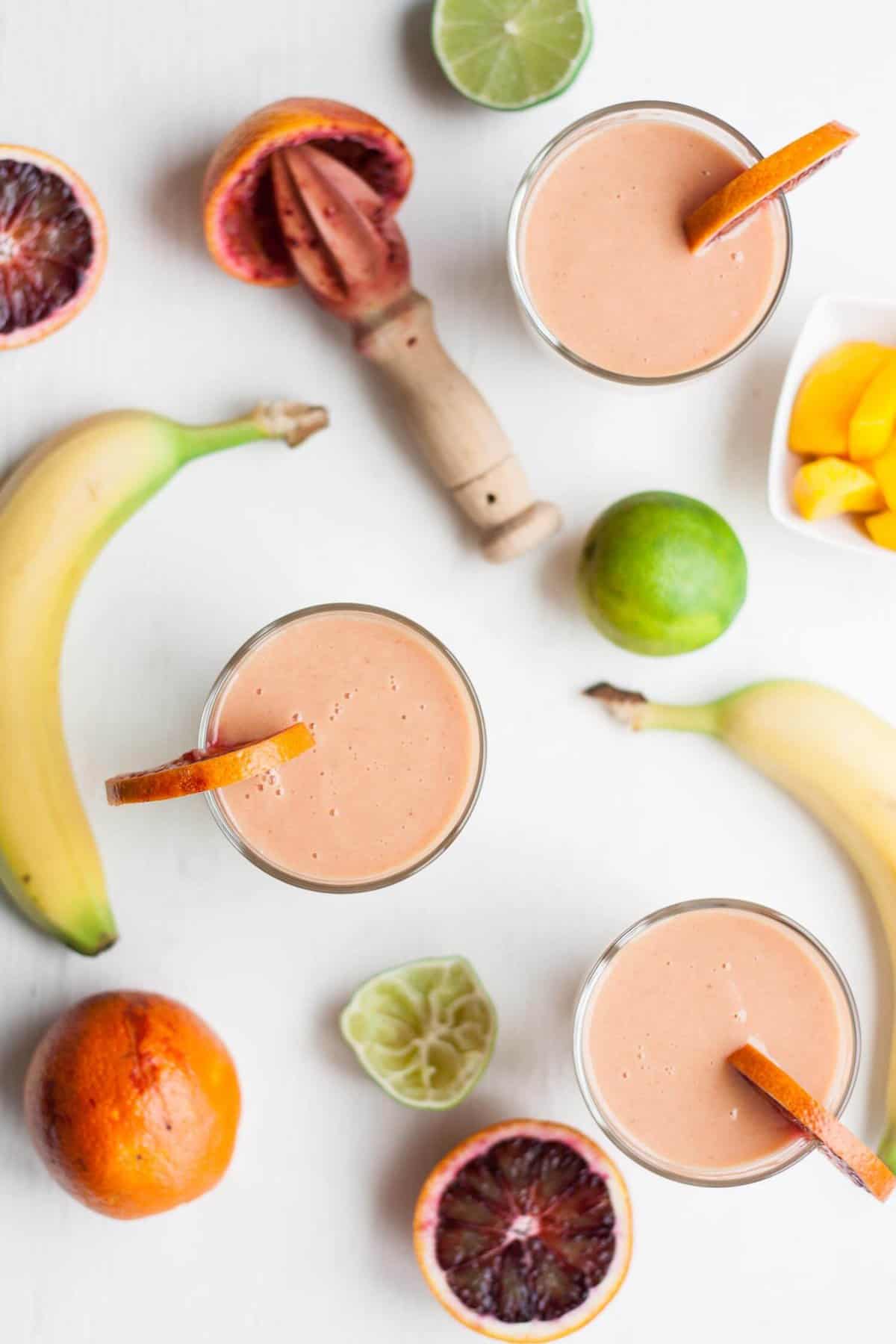 Overhead of three orange and mango smoothiees with fruit around.
