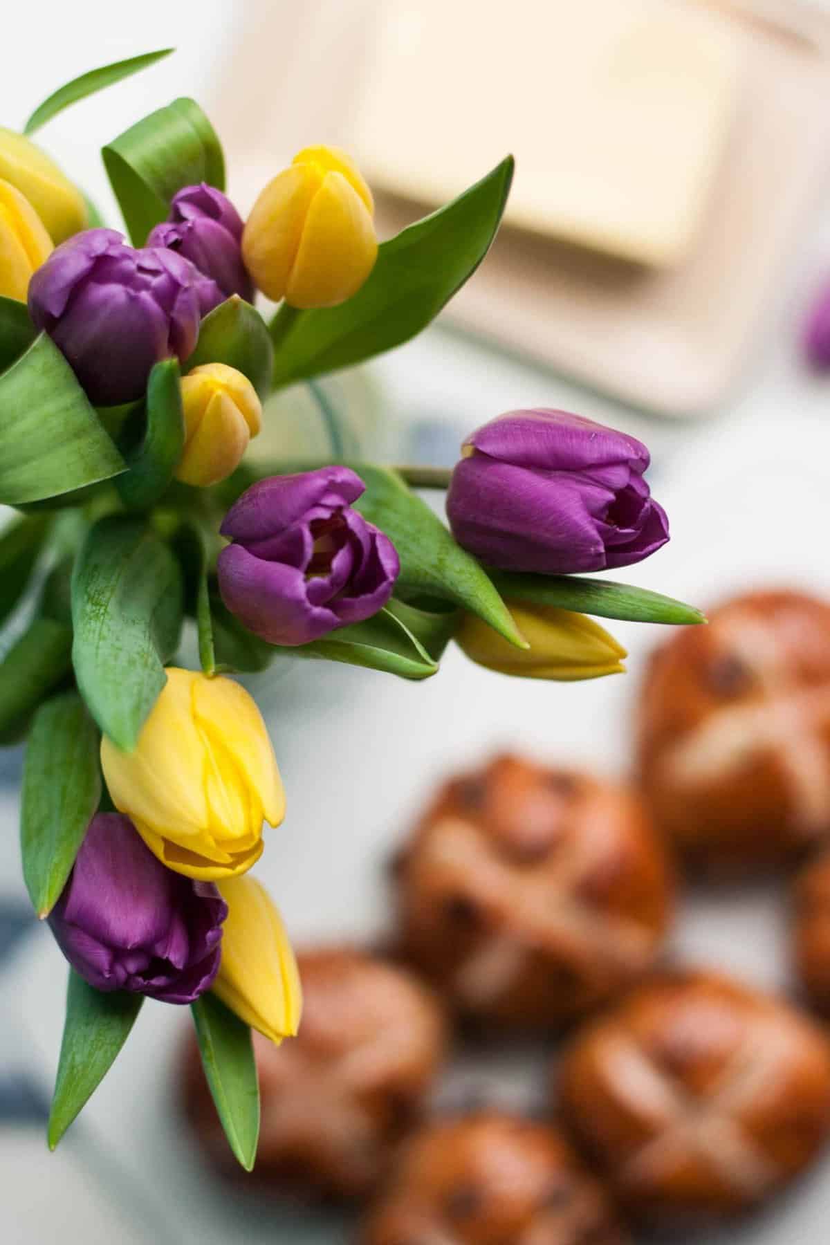 Tulips in a vase with hot cross buns in the background.
