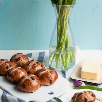 Hot cross buns on a cutting board with napkin and vase of flowers.