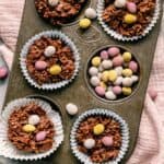 Chocolate cornflakes cakes in a baking tin with mini chocolate eggs around.